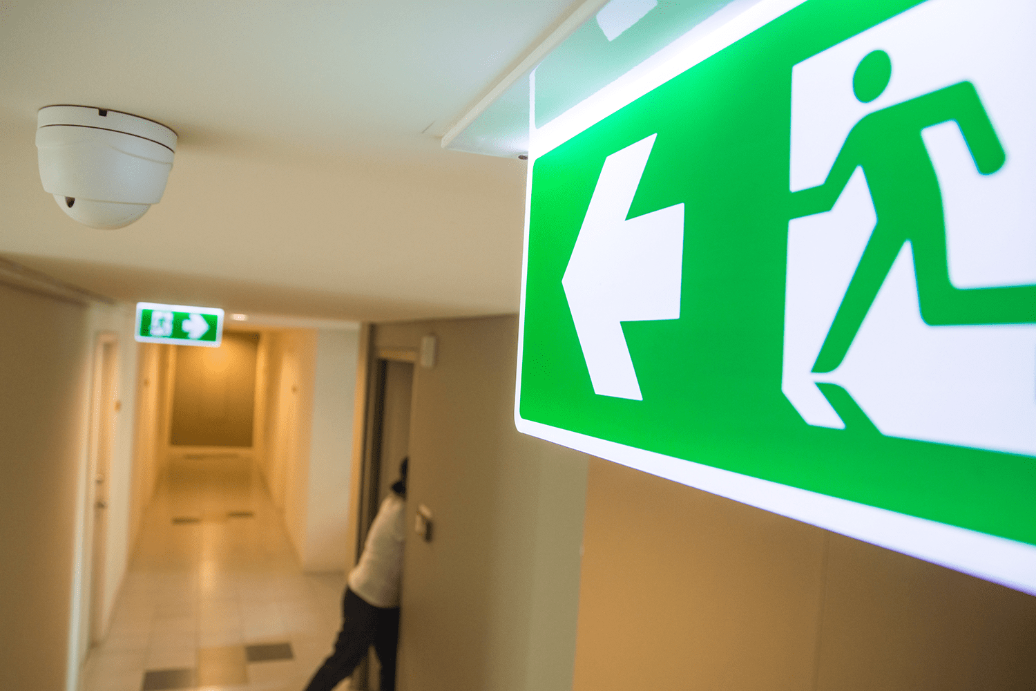 Fire exit signs in a corridor with woman escaping